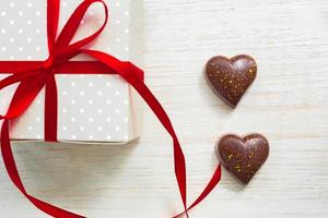 Greeting card for st valentines day. Chocolate sweets in heart shape and giftbox with red celebration ribbon on wooden background photo