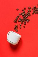 Top view of fresh roasted coffe beans and whte cup on red background. Flat lay. photo