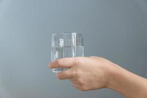 mujer sosteniendo un vaso de agua en la mano sobre fondo gris foto