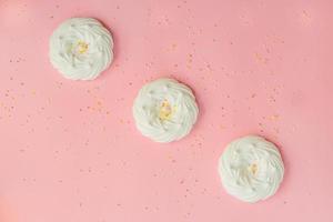 top view of homemade white air meringues and confectionery decorations on pink background photo