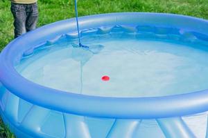 limpieza de piscina jardín. el chico intenta atrapar la bola roja con una red skimmer foto