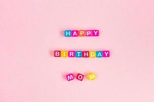 inscripción de feliz cumpleaños mamá hecha de cuentas de cubo de colores con letras. concepto de fondo rosa festivo con espacio de copia foto