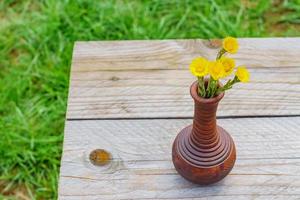 Freshly cut yellow coltsfoot flowers in clay vase on wooden table outdoors. Rustic style. photo