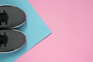 A pair of sport shoes on multiclored surface. New black and white woman sneakers on pink and blue pastel background with copy space. Top view, flat lay photo