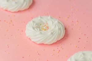 merengues caseros de aire blanco y decoraciones de confitería sobre fondo rosa foto