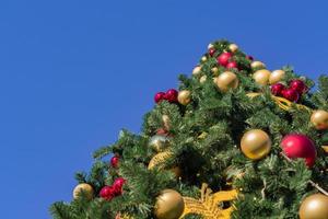 Christmas and New Year holidays background.  Christmas tree decorated with balls and garlands against blue sky, bottom view photo