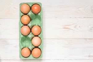 top view of raw brown chicken eggs in egg carton box on wooden table. photo