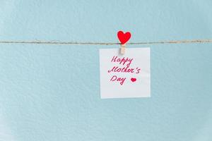 Pinned paper with happy mothers day inscription hanged on cord against blue background photo