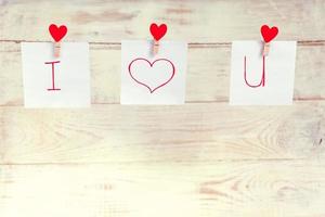 Red Valentine's love hearts pins hanging on natural cord against white wooden background. I love you inscription on paper pieces. photo