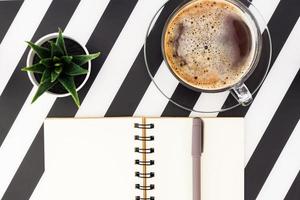 Stylish minimalistic workspace with notebook, pen, cup of coffee and succulent on striped black and white background. Flat lay style Top view. photo
