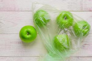 Fresh green apples in plastic bag on wooden table. environmental concept of non-ecological use of plastic photo