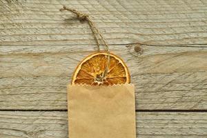 decoración navideña rodaja de naranja seca en paquete de papel artesanal sobre fondo de madera, vista superior, capa plana mínima foto