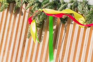 wooden fence decorated by christmas branches covered with snow with multicolored satin ribbons photo