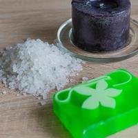 Pile of sea salt, soap bar and black candle on wooden table. Natural ingredient for spa and exfoliation. photo