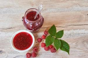 Raspberry jam and fresh raspberry with green leves on a rustic wooden table photo