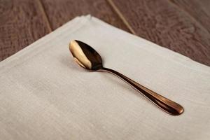 close up of cloth napkin of beige color and served tea spoon on wooden table. photo