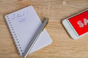 close up view of office desk with white smartphone with sale text, note and pen. Technology business online shopping concept photo