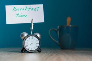 Alarm clock and banner with handwritten phrase breakfast time on wooden table. Time management concept. photo