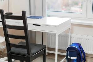 el lugar de trabajo del estudiante en casa. escritorio blanco y silla negra cerca de la ventana. foto