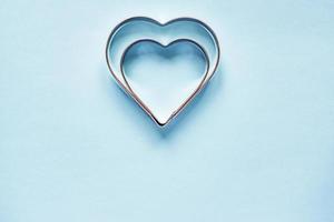 Two metal cookie cutters in heart shape on light blue background with copy space photo