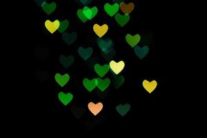 Bokeh de corazones multicolores de colores verdes y amarillos sobre fondo negro. textura para vacaciones foto