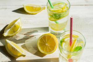 glass of homemade lemonade with lemons, mint and paper straws on wooden rustic background. Summer refreshing beverage. hard shadows photo