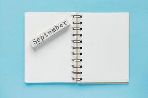 Clean spiral note book for notes and messages and september wooden calendar bar on blue background. Minimal business flat lay photo