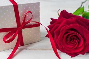 Beige polka dot gift box with red ribbon bow and bautiful red roses on wooden background. Greeting card for holiday. photo