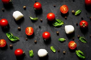 Mozzarella cheese balls with fresh basil leaves and cherry tomatoes, ingredients for Italian Caprese salad, on a black background. Eating pattern photo