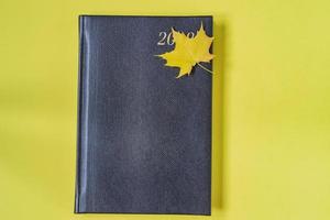 cuaderno de cuero de reptil falso de color negro con hoja de arce como marcador sobre fondo amarillo foto