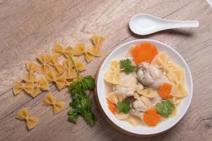 Macaroni soup with chicken thighs in clear broth with carrots.on an rustic old wood background. photo