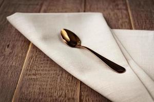 Close up of textile beige napkin and served tea spoon on wooden table. photo