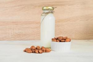 leche de almendras casera en una botella y nueces en un tazón de porcelana blanca sobre fondo de madera foto