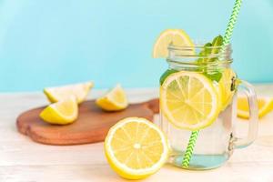 Mason jar glass of homemade lemonade with lemons, mint and green paper straw on wooden rustic table and blue background. Summer refreshing beverage. photo