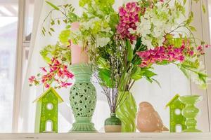 Spring interior decoration in green and pink colors. Blooming white and pink flowers, statuette of bird, candle sticks and birds houses on a cabinet photo