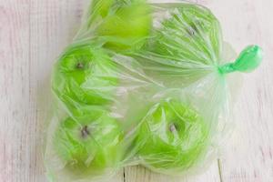 Fresh green apples in plastic bag on wooden table. environmental concept of non-ecological use of plastic photo