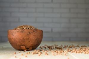 Dry buckwheat in brown clay bowl on wooden table. gluten free grain for healthy diet photo