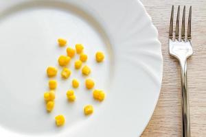 Close up of sweet corn i and steel fork in white plate on wooden table photo