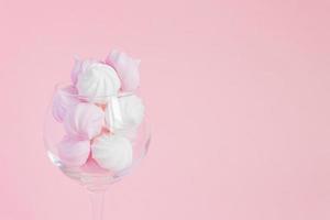 White and pink twisted meringues in  a vine glass on pink background. French dessert prepared from whipped with sugar and baked egg whites. Greeting card with copy space photo