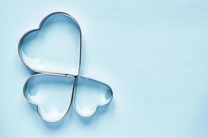 Three metal cookie cutters in heart shape on light blue background with copy space photo