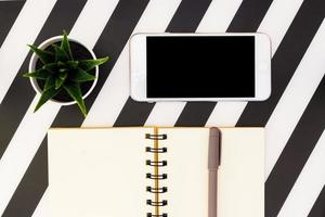 mesa de oficina en blanco y negro con cuaderno en blanco, teléfono inteligente y suculento. vista superior con espacio de copia, plano. foto