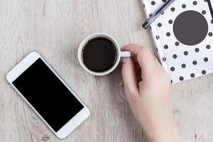 Business and office concept - black and white polka dot cover notebook, smartphone and cup of black coffee on wooden table. top view. photo