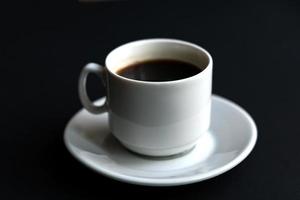 primer plano de una taza de café blanca sobre fondo negro. enfoque suave foto