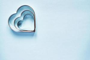 tres cortadores de galletas de metal en forma de corazón sobre fondo azul claro con espacio de copia foto