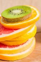 stack of slice of oranges, lemons, kiwi, grapefruit on wooden background photo