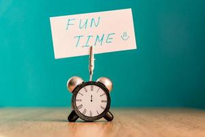 Alarm clock and banner with handwritten phrase fun time on wooden table. Time management concept. photo