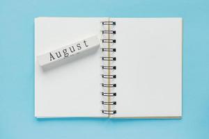 Clean spiral note book for notes and messages and august wooden calendar bar on blue background. Minimal business flat lay photo