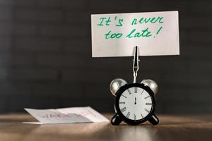 Alarm clock and banner with handwritten phrase Its never too late on wooden table. Time management concept. photo