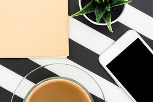 Stylish minimalistic workspace with notebook, pen, cup of coffee, smartphone and succulent on striped black and white background. Flat lay style Top view. photo