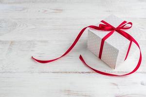 Beige polka dot gift box with red ribbon bow on wooden background with copy space. photo